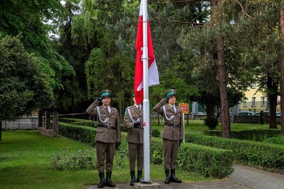 funkcjonariusze straży granicznej oddają honor podczas wciągania flagi polski na maszt. jeden z nich wciąga flagę.
