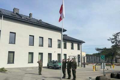 funkcjonariusze straży granicznej oddają honor przed flaga Polski. w tle budynek Placówki SG w Tarnowie.