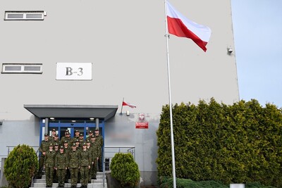 funkcjonariusze straży granicznej stojący na schodach przed wejściem do Placówki SG w Krakowie. po prawej stronie znajduje się maszt z flagą Polski.