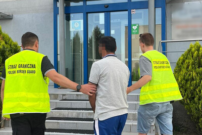 Dwóch funkcjonariuszy straży granicznej bez munduru a w odblaskowych kamizelkach wprowadza do siedziby placówki straży granicznej zatrzymanego obywatela Turkmenistanu.