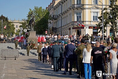 Na zdjęciu w tle widoczny pomnik mężczyzny na koniu. Obok niego mężczyźni w mundurach wojskowych trzymający wartę. Przed pomnikiem widoczna tyłem liczna grupa osób w różnym ubraniu. Za pomnikiem rząd biało - czerwonych flag.
