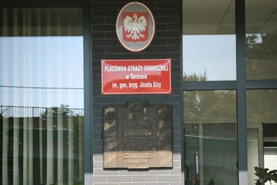 Na zdjęciu tablica pamiątkowa wmurowana w fasadę budynku. Ponad nią godło Polski - biały orzeł w koronie na czerwonym tle oraz tabliczka informująca o siedzibie placówki Straży granicznej w Tarnowie.