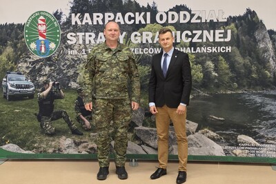 dwóch mężczyzn w tym jeden funkcjonariusz stoją na tle baneru z napisem karpacki oddział straży granicznej