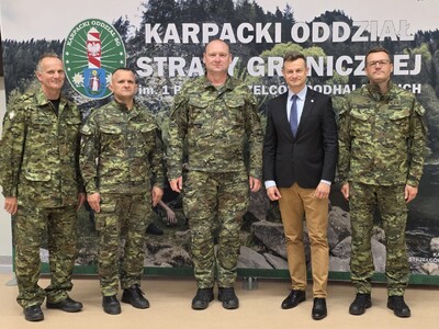 Pięciu mężczyzn w tym  czterech funkcjonariuszy stoi na tle baneru z napisem karpacki oddział straży granicznej
