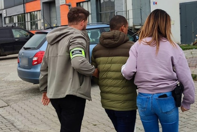 Dwie osoby, kobieta i mężczyzna prowadzą pod ręce osobę zatrzymaną.