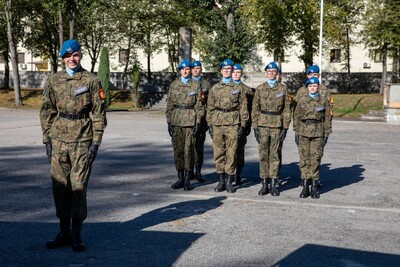 Grupa młodych żołnierzy w mundurach polskiej armii i niebieskich beretach stoi na zewnątrz w szyku. Jeden żołnierz uśmiecha się na pierwszym planie