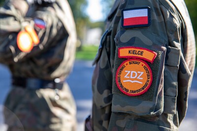 Zbliżenie na rękaw munduru polskiego żołnierza, ukazujące naszywki: polską flagę, napis &#039;KIELCE&#039; oraz logo &#039;Zarządu Doskonalenia Zawodowego w Kielcach ZDZ.