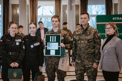 dwie uczennice i jeden uczeń stoją w towarzystwie nauczycielki i wręczającego nagrodę funkcjonariusza sg