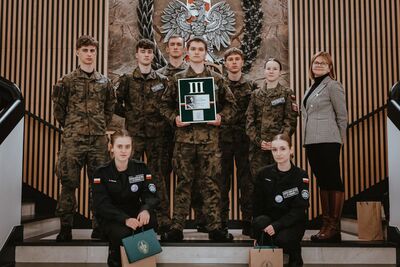 drużyna z tymbarku wraz z nauczycielką stoją na schodach w komendzie głównej straży granicznej , w tle logo sg