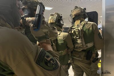 Funkcjonariusze ZIS w oporządzeniu  bojowym z tarczą balistyczna poruszają się na terenie terminala w zwartej grupie szturmowej