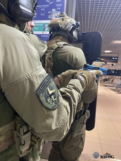 Funkcjonariusze ZIS w oporządzeniu  bojowym z tarczą balistyczna poruszają się na terenie terminala w zwartej grupie szturmowej
