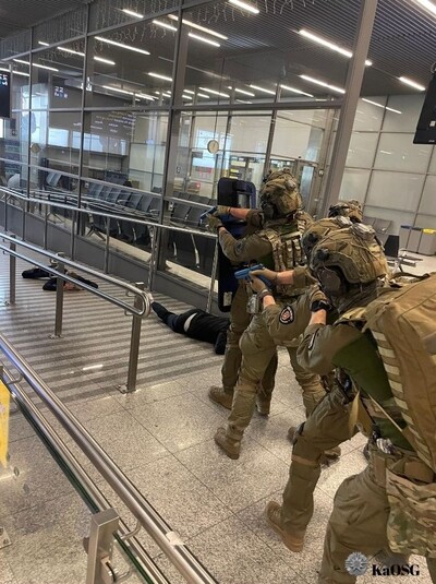 Funkcjonariusze ZIS w oporządzeniu  bojowym z tarczą balistyczna poruszają się na terenie terminala w zwartej grupie szturmowej