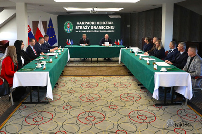 Na zdjęciu widać grupę ludzi po prawej i po lewej stronie siedzących przy stole na wprost siedzi dwóch mężczyzn i omawiają coś