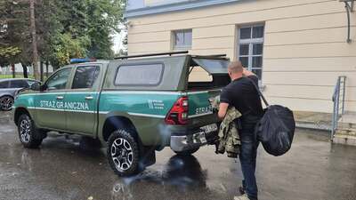 Funkcjonariusz pakuje ekwipunek do bagażnika zielonego radiowozu terenowego marki Toyota z napisem "Straż Graniczna".