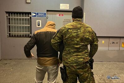 Dwóch mężczyzn stoi tyłem przed budynkiem.