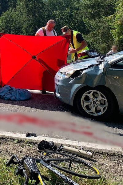 Funkcjonariusz SG i strażak udzielają pomocy poszkodowanemu w wypadku mężczyźnie. Na pierwszym planie rozbity samochód i  szyba przednia oraz leżący na poboczu uszkodzony rower. Na jezdni ślady krwi, miejsce udzielania pomocy zakryte jest specjalnym stelażem.