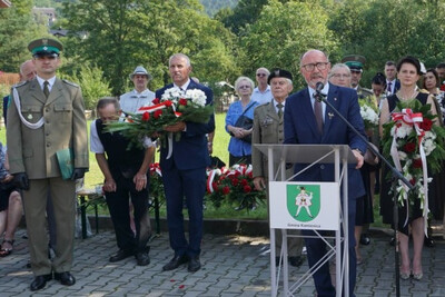 Miejsce uroczystości, plac przed pomnikiem partyzantów, uczestnicy uroczystości słuchają przemawiającego.
