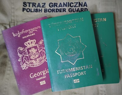 W tle napis na koszuli służbowej o treści Straż Graniczna Polish Border Guard. na niej położone trzy paszporty. Pierwszy (bordowy) zatrzymanego obywatela Gruzji, a dwa kolejne (zielone) dwoje obywateli Turkmenistanu.