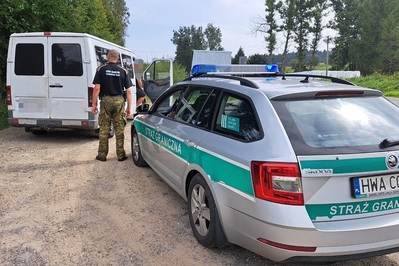 Samochód oznakowany z napisem Straż Graniczna, funkcjonariusz kontroluje pasażerów busa, którym podróżują cudzoziemcy.