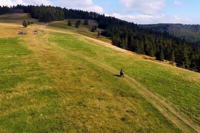 Funkcjonariusze KaOSG współdziałają i pomagają Funkcjonariusz Straży Granicznej poruszający się motocyklem służbowym po szlaku Gorczańskiego Parku Narodowego. widok na szeroką łąkę oraz kompleks leśny parku.