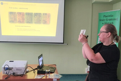 Przedstawicie NBP szkolili funkcjonariuszy i pracowników KaOSG sala w której znajduje się ekran na którym pokazywane są slajdy ze szkolenia. jest tam również specjalista omawiający zagadnienia dotyczące szkolenia.