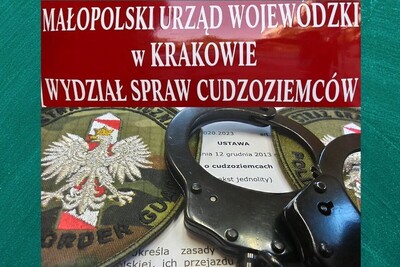 Uzbek i Mongoł nielegalnie na terytorium RP Tablica z napisem Małopolski Urząd Wojewódzki w Krakowie Wydział Spraw Cudzoziemców pod nią kajdanki oraz dwa emblematy Straży granicznej znajdujące się na wersji papierowej ustawy o cudzoziemcach.  całość na zielonym tle.