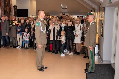 Nowi funkcjonariusze SG ślubowali w obecności Sztandaru KaOSG Sala odpraw. Na pierwszym planie funkcjonariusz składa meldunek komendantowi Karpackiego Oddziału Straży Granicznej. W tle rodziny osób składających ślubowanie.