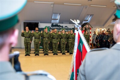 Nowi funkcjonariusze SG ślubowali w obecności Sztandaru KaOSG Sala odpraw. W tle grupa 30 funkcjonariuszy z podniesionymi do ślubowania dłońmi składa ślubowanie. Na pierwszym planie część sztandaru KaOSG.