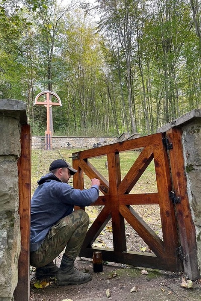 VIII akcja sprzątania cmentarzy z okresu I wojny światowej funkcjonariusz straży granicznej malujący wejście na cmentarz wojskowy.