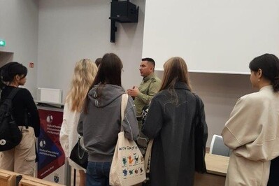 Sala wykładowa. Funkcjonariusz Straży Granicznej stoi z grupą studentów i odpowiada na ich pytania.