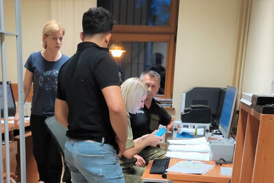 Pomieszczenia Placówki SG w Zakopanem. Dwie funkcjonariuszki i jeden funkcjonariusz prowadzą czynności służbowe wobec zatrzymanego cudzoziemca. Dwoje funkcjonariuszy siedzi przy biurku. Cudzoziemiec i funkcjonariuszka w ubraniu cywilnym stoją przy biurku. Po lewej stronie kraty od wejścia do pomieszczenia.