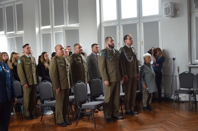 Uczestnicy premiery książki stoją na baczność i śpiewają Hymn państwowy. Jest to około 100 osób.