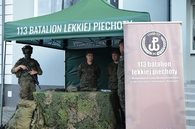 Czterech umundurowanych żołnierzy 113 Batalionu lekkiej piechoty stoi pod namiotem, w którym prezentowany jest sprzęt służbowy i uzbrojenie. Na stole leży hełm i broń.