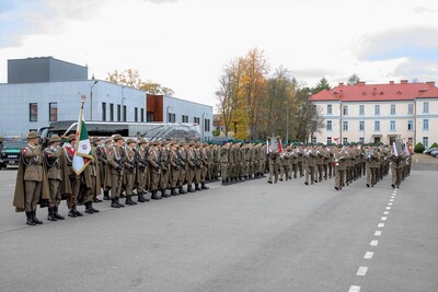 Plac apelowy w siedzibie Karpackiego Oddziału Straży Granicznej. W tle budynki Oddziału. Pododdziały biorące udział w uroczystości 105.  rocznicy odzyskania niepodległości przez Nowy Sącz stoją w szyku. Przed nimi maszeruje grająca Orkiestra Reprezentacyjna Straży Granicznej, prowadzona przez tamburmajora.