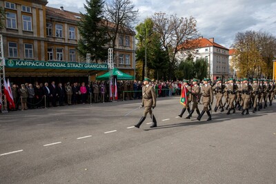 Na pierwszym planie dowódca Kompani Reprezentacyjnej Straży Granicznej prowadzący kompanię podczas defilady. W tle zaproszeni goście oraz wszyscy zebrani podczas uroczystości obserwujący defiladę.