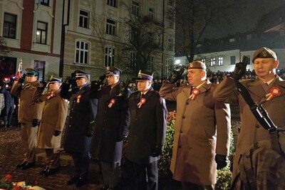Siedmiu przedstawicieli służb mundurowych oddaje honor po złożeniu wieńca kwiatów. Wśród nich Komendant Placówki SG w Tarnowie – kapitan SG Paweł Wolak. W tle kamienice tarnowskie i uczestnicy uroczystości.