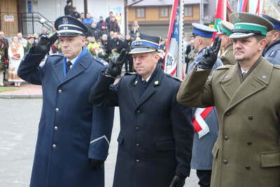 Rynek w Białym Dunajcu. Przedstawiciele służb mundurowych oddają honor po złożeniu kwiatów. Wśród nich Komendant Placówki SG w Zakopanem – podpułkownik SG Andrzej Karkoszka.  W tle poczty sztandarowe oraz uczestnicy uroczystości, część w góralskich tradycyjnych strojach.