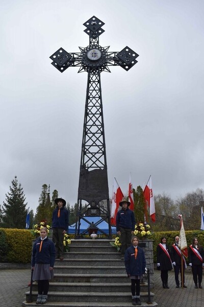 Plac przy Krzyżu papieskim – kopia z Giewontu - przy Sanktuarium Narodowym na Krzeptówkach. Na schodach pod krzyżem harcerze pełnią wartę honorową. Powiewają biało-czerwone flagi. Po prawej stronie stoi poczet sztandarowy.
