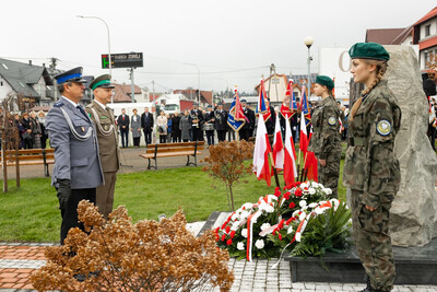 Jabłonka. Przed pomnikiem stoi funkcjonariusz z Placówki SG w Zakopanem w towarzystwie policjanta. Powiewają biało-czerwone flagi. Przed pomnikiem młodzież w mundurach pełni wartę honorową, na ziemi leżą wiązanki biało-czerwonych kwiatów. W tle uczestnicy uroczystości.