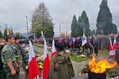 Cmentarz komunalny w Starym Sączu. Przy kwaterze z grobami legionistów zgromadziło się bardzo wielu uczestników uroczystości rocznicowych, poczty sztandarowe i delegacje służb mundurowych. Wartę pełnią harcerze. Płonie duży znicz, powiewają biało-czerwone flagi.