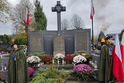 Cmentarz komunalny w Starym Sączu. Przy kwaterze z grobami legionistów wartę pełnią harcerki. Płoną dwa duże znicze, powiewają biało-czerwone flagi. Pomnik ustrojony jest wieloma chryzantemami.