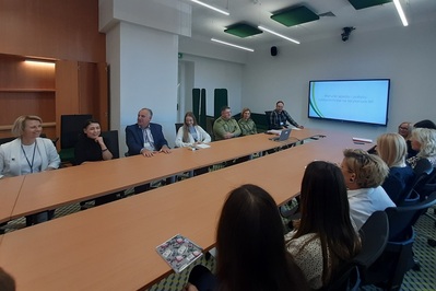 Sala szkoleniowa w Małopolskim Urzędzie Wojewódzkim Delegatura w Nowym Sączu. Uczestnicy szkolenia i prelegenci siedzą przy dużym stole konferencyjnym. Na ścianie tablica interaktywna, na której wyświetlany jest slajd tytułowy szkolenia o treści: Warunki wjazdu i pobytu cudzoziemców na terytorium RP.