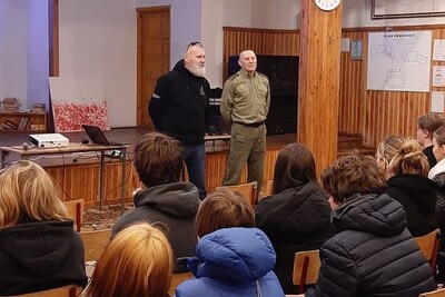 Narkotyki i handel ludźmi tematami prelekcji dla zakopiańskiej młodzieży funkcjonariusz straży granicznej , którego zapowiada jeden z organizatorów spotkania.  przed nimi siedzą uczniowie biorący udział w prelekcji.