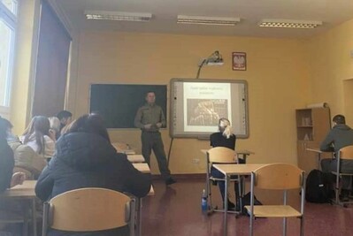 Narkotyki i handel ludźmi tematami prelekcji dla zakopiańskiej młodzieży funkcjonariusz straży granicznej prowadzący prelekcje. przed nim siedzą uczniowie biorący udział w prelekcji. za funkcjonariuszem slajd z informacjami , które są omawiane podczas spotkania.