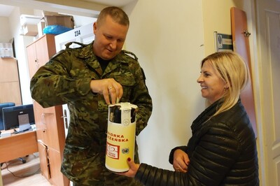 Pomieszczenia KaOSG. Funkcjonariusz wrzuca zbierającej do puszki przedstawicielce Związku Zawodowego Pracowników MSWiAP datek pieniężny.
