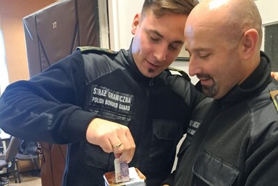 Pomieszczenia Orkiestry reprezentacyjnej SG. Funkcjonariusz wrzuca zbierającemu do puszki przedstawicielowi Związku zawodowego Funkcjonariuszy SG datek pieniężny.