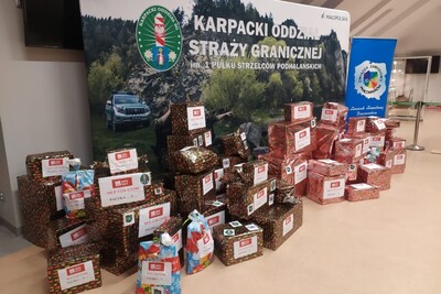 Sala Tradycji KaOSG  przed banerem  z napisem karpacki oddział straży granicznej leży około 70  kolorowo zapakowanych prezentów, przeznaczonych dla dwóch rodzin, wybranych do obdarowania w ramach akcji szlachetna paczka .