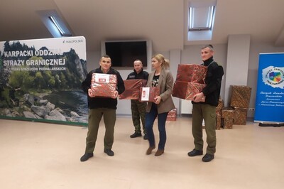 Sala Tradycji KaOSG jedna pracownica i trzech funkcjonariuszy wynosi przygotowane paczki. W tle baner z kolorowym logotypem i napisem  związek zawodowy pracowników ministerstwa spraw wewnętrznych i administracji publicznej oraz drugi baner z  napisem karpacki oddział straży granicznej.  W tle pozostałe do wyniesienia kilka paczek.