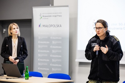 Funkcjonariuszka SG przemawia do mikrofonu. Obok niej stoi moderator konferencji