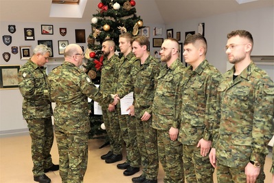 Sala Tradycji KaOSG. W szeregu stoi 6 funkcjonariuszy SG w umundurowaniu polowym. Pułkownik  Marcisz wręcza akt mianowania jednemu z funkcjonariuszy SG. Towarzyszy mu naczelnik wydziału kadr i szkolenia, który podaje dokumenty.